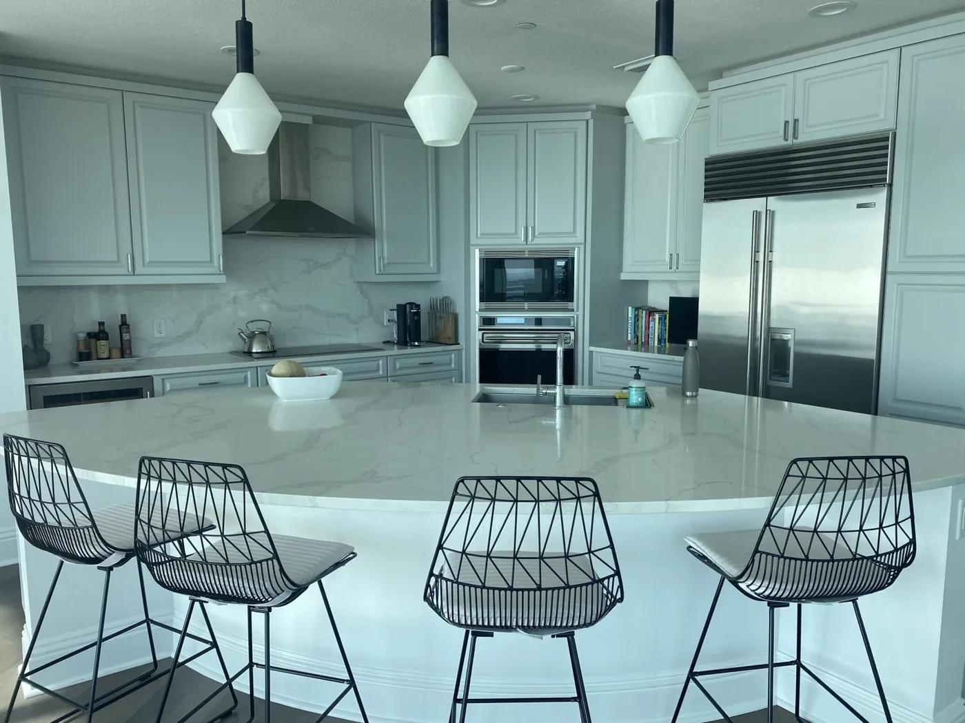 White kitchen with a marble island, pendant lights and wire bar stools