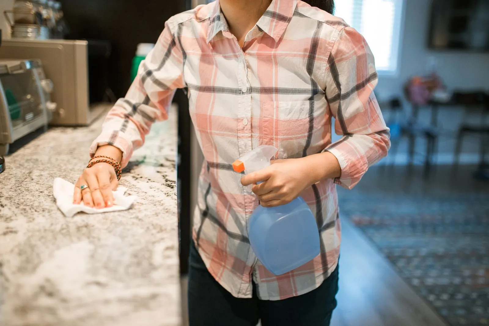 A woman wiping down a granite kitchen counter with a cloth and a spray bottle